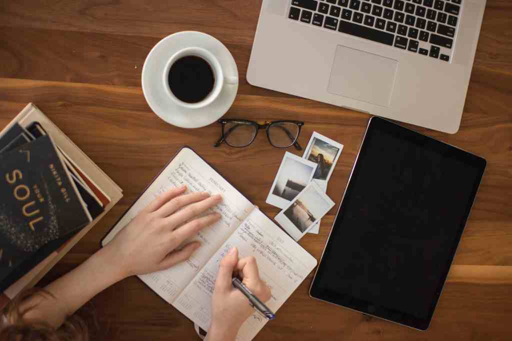 A person writing in a notebook while surrounded by business items