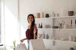 A woman holding two white shopping bags smiling while in a store