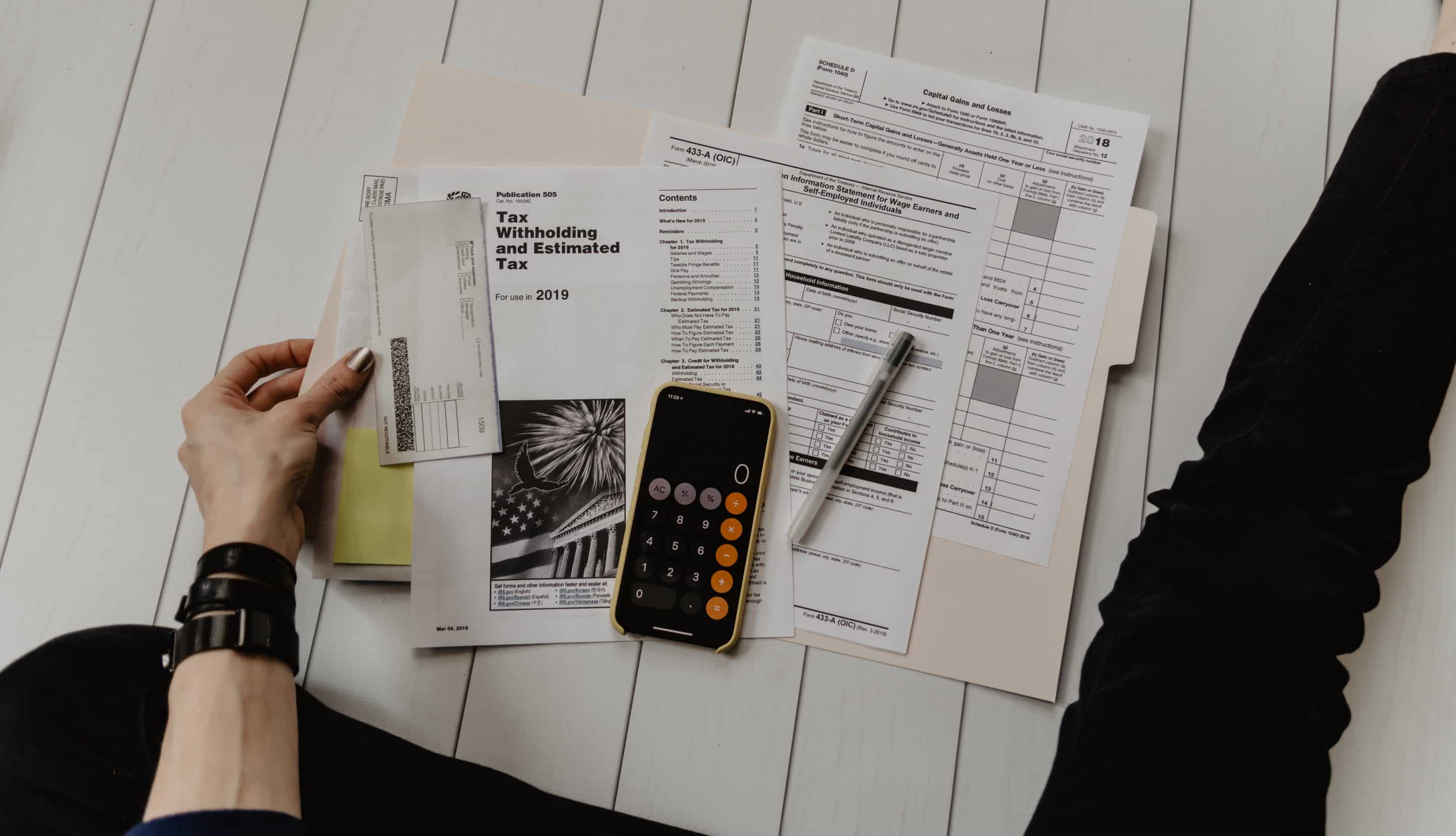 A woman's hand holding business papers sitting next to a calculator and pen