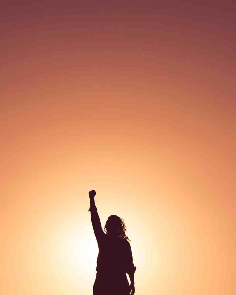 A person far away, blurred by a very bright background, holding one fist up to the sky