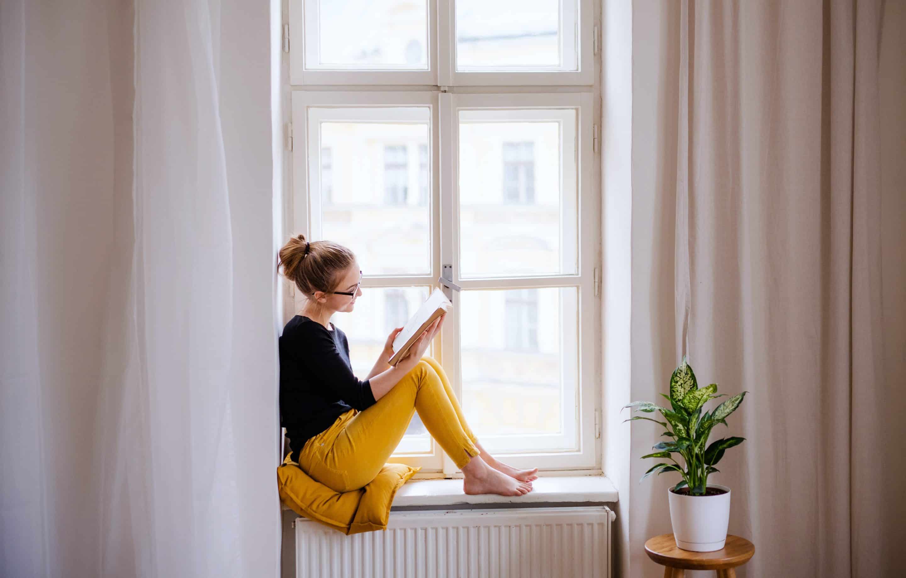 Woman sitting on a windowsill reading a book
