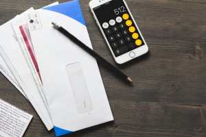 A large amount of bills piled up on a desk next to a pencil and a calculator