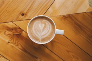 A cup of coffee sitting on a desk with creamer on the top