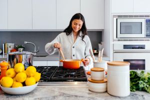 A woman in the kitchen stirring food in an orange pot