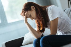 A woman sitting on a couch with her hand on her head looking upset