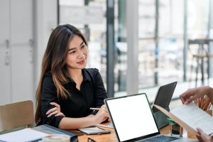 A woman sitting at the office smiling to someone across the table from her while she works