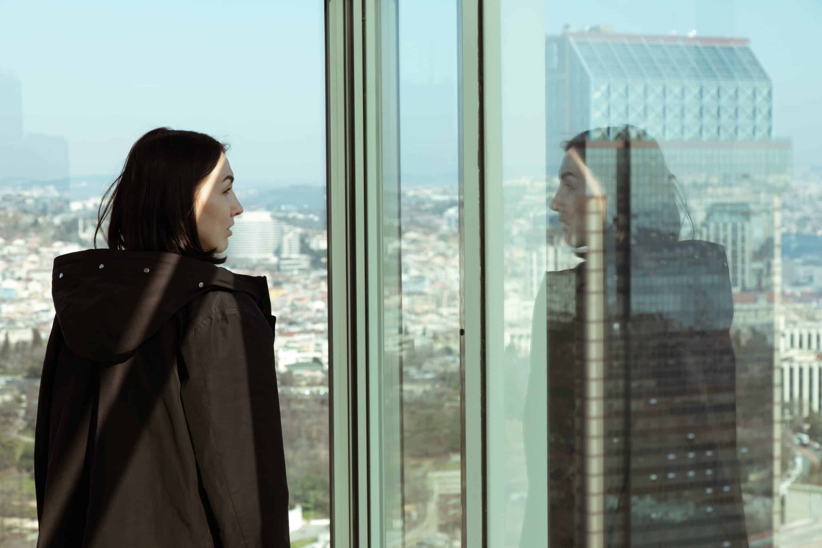 Woman staring at her reflection in a store glass window with a big city in the background