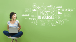 A woman sitting on a stool with a laptop and her feet up with wording next to her that says Investing in yourself