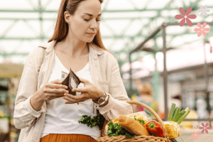 A woman with groceries in a basket and her hands in her wallet with money coming out