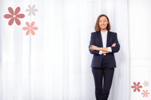 Woman in a black business suit with her arms crossed smiling against a solid white background