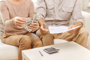 Two people sitting on the couch holding money with a calculator, pen, and paper in front of them