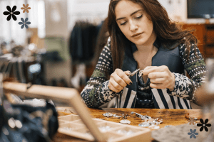 A dark-haired woman working on creating jewelry with multiple items on a desk