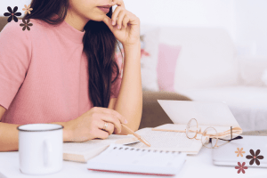 Woman in a pink sweater looking down at a notepad while holding a pencil