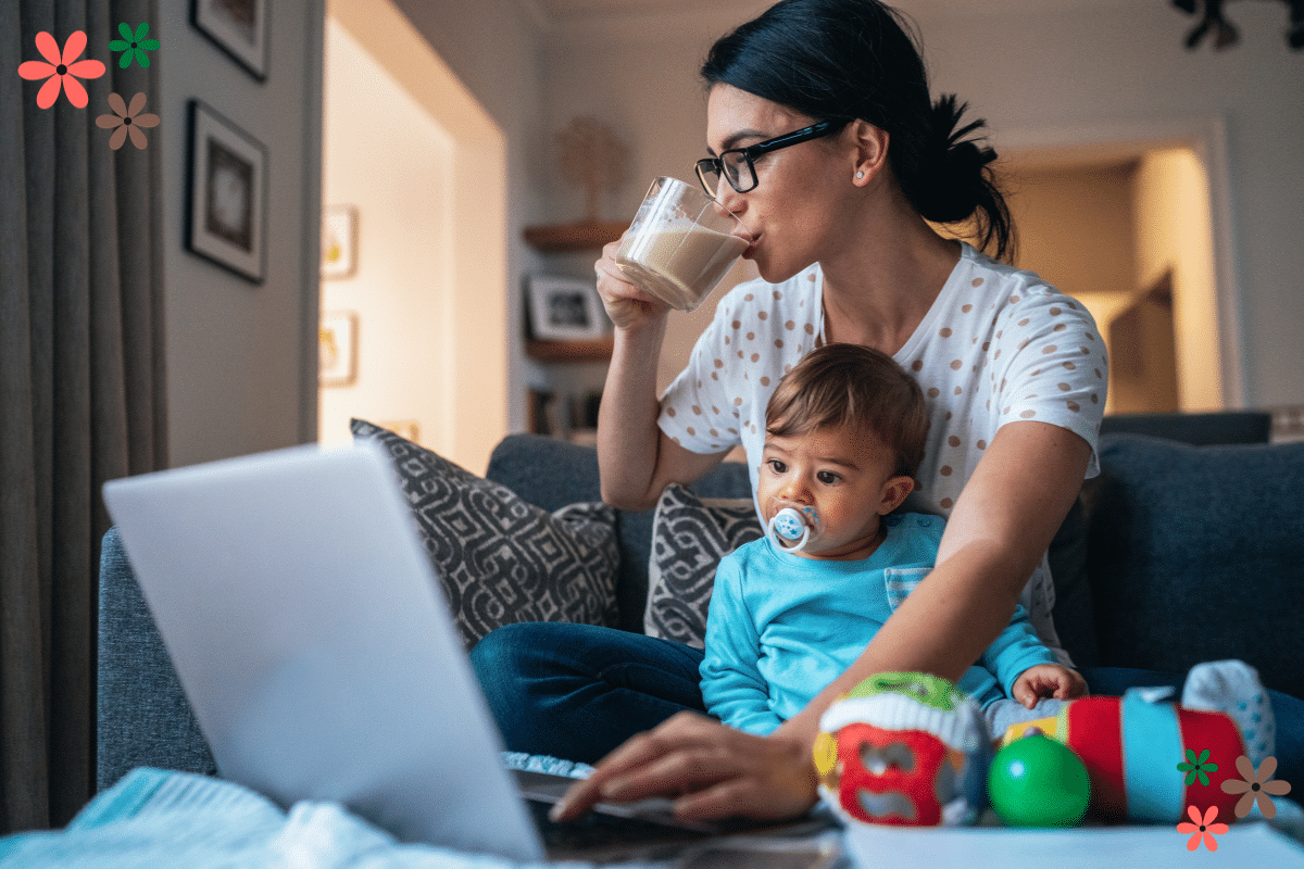 mom guilt A mom drinking a coffee while looking at a laptop and holding a toddler in her lap