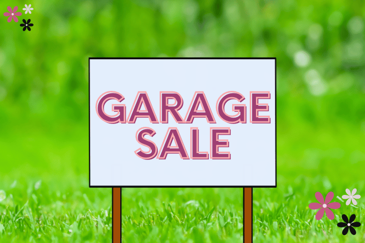 Garage sale Sign sitting on green grass that reads Garage Sale in pink